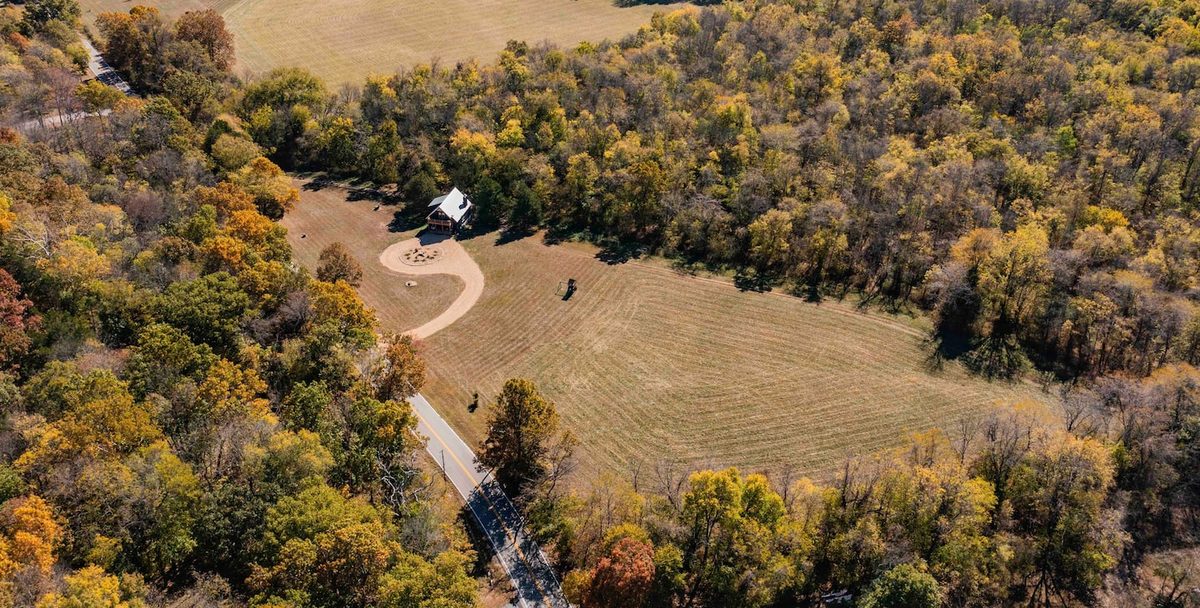 Aerial view of the 90-acre property with the cabin set among fields and forest